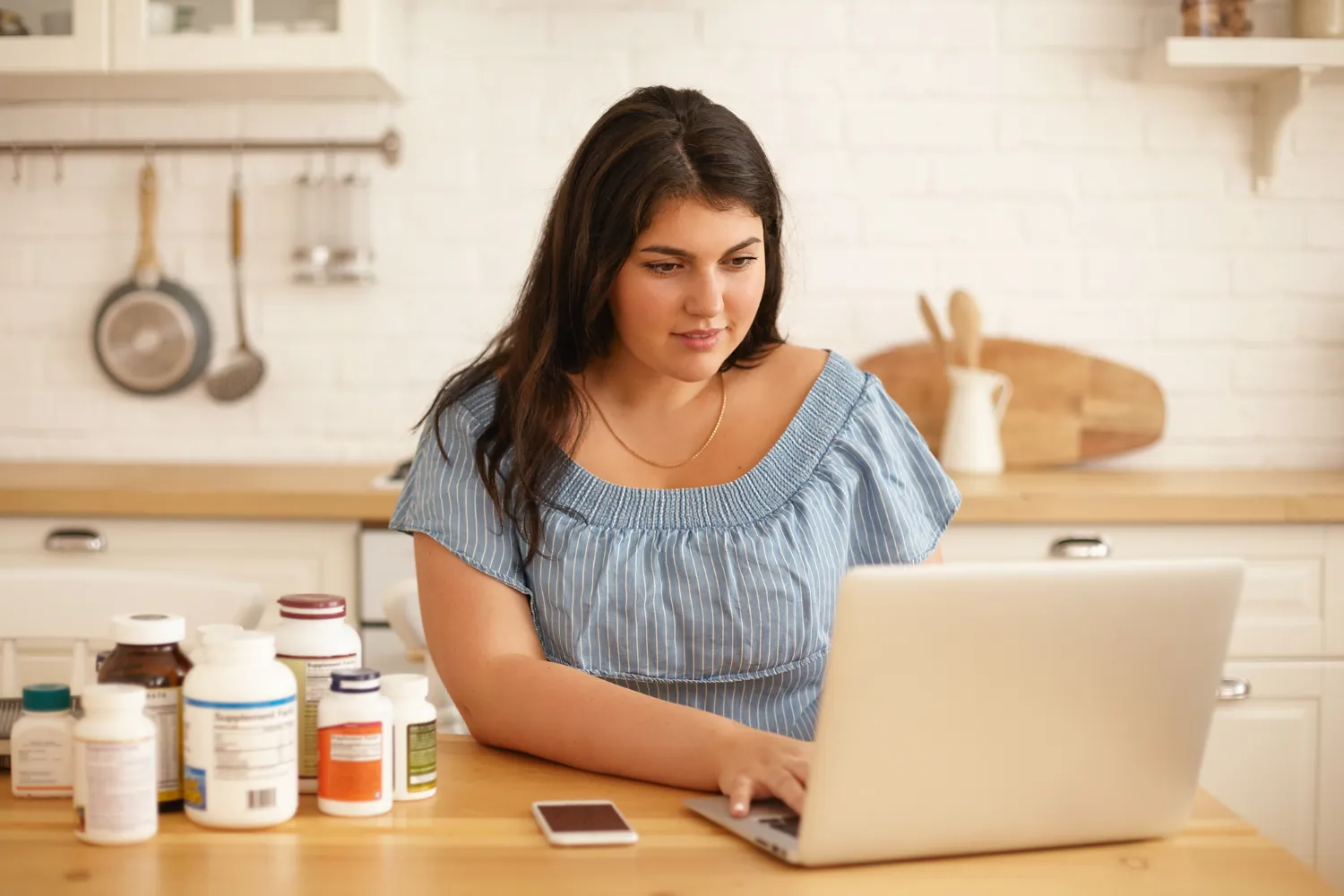 Person researching weight management medications on a laptop with prescription bottles nearby, representing weight management pharmacy services and personalized compounded weight loss treatments.
