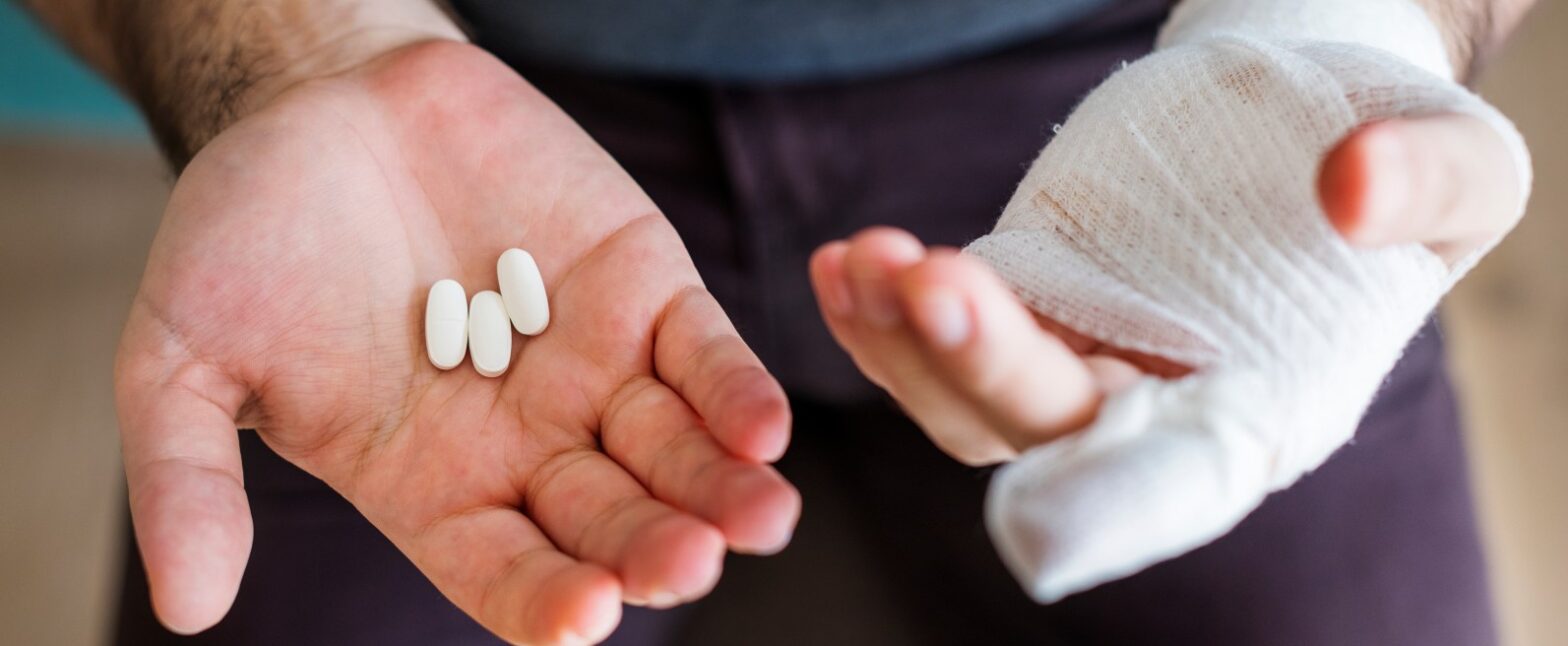 Person holding prescription pills with a bandaged hand during injury recovery
