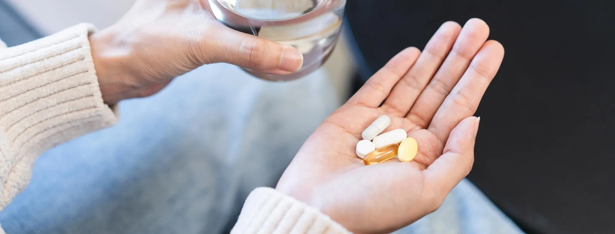 Person holding multiple oral medications and a glass of water, representing personalized erectile dysfunction treatments through a compounding pharmacy for individualized ED care.